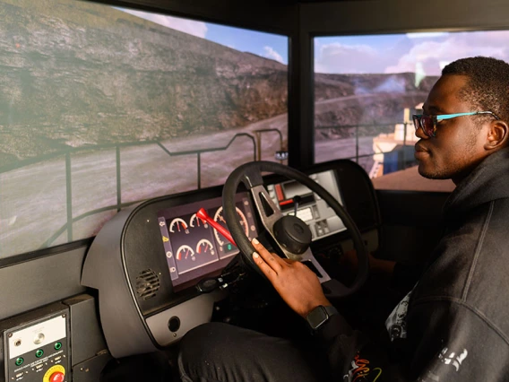 a student sits in a simulator including a vehicle seat and dashboard and screens