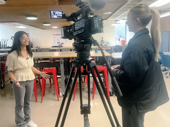 A student speaks to a reporter with a camera on a tripod