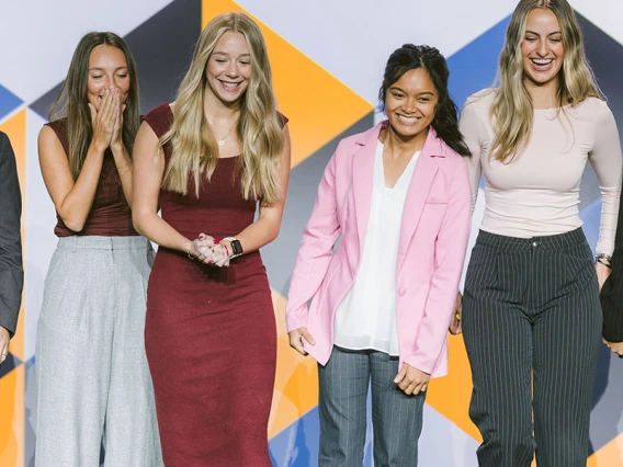 Six people on a stage react to winning an award.