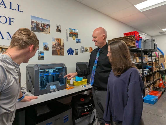 Three people surround a piece of equipment in a classroom