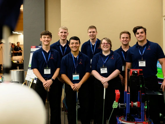 Six men and one woman pose for a photo next to a golfing robot.
