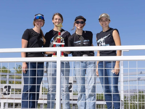Four high school students pose outdoors with a trophy.