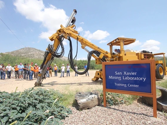 A yellow mining shovel vehicle sits behind a blue sign.
