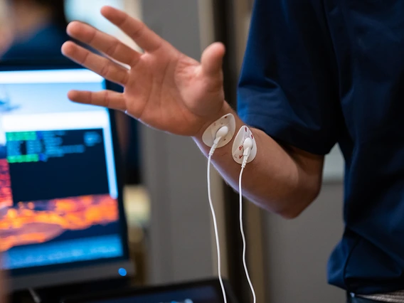 A man in a blue polo demonstrates a medical device on his wrist.