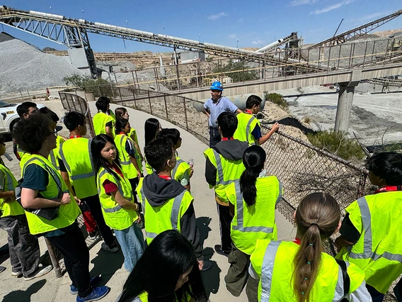 A group of students in yellow vests look over a railing at an open mine pit.