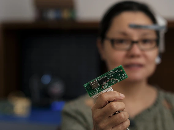 A woman with dark brown hair holds up a computer chip.