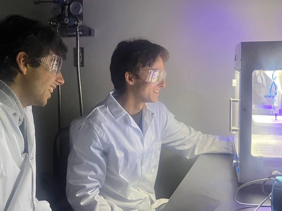 Two students with dark hair look at a 3D printer.