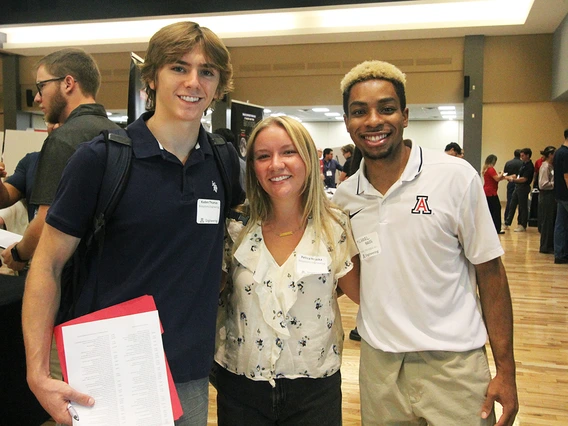 Three students smile for a photo in a large ballroom.
