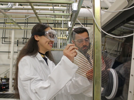 Two students wearing lab coats and goggles in a lab.