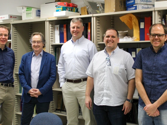 Five men pose for a photo in front of a bookshelf