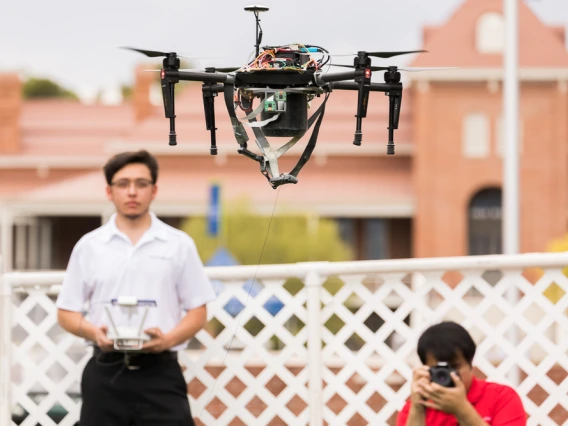 A student in a white polo shirt flies a tethered drone outside Old Main at Engineering Design Day