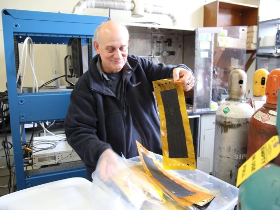 Dominic Gervasio smiles while he sifts through a stack of composite membranes, paper-thin black material with transparent yellow borders, about 1.5 feet by six inches.