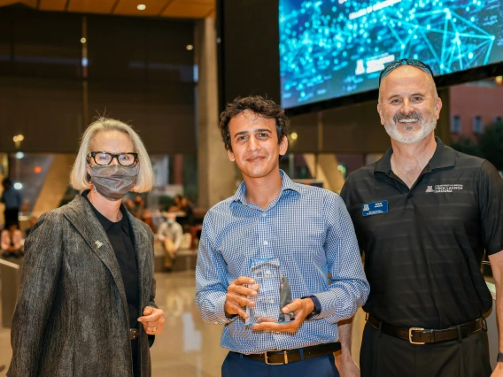 A woman and two men smile for a photo. Sahand Sabet, center, holds a glass award.