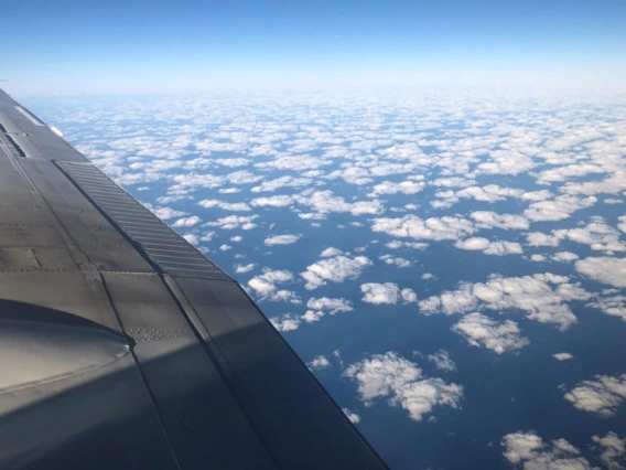 photo taken from a plane showing cumulus clouds from above. The wing of the plane is visible in the left of the frame