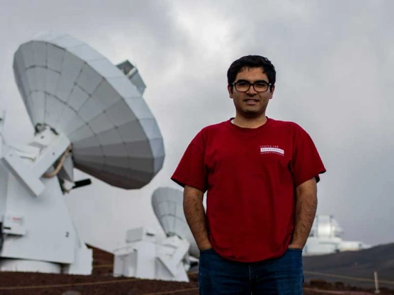 Arash Roshanineshat stands in front of a big, white satellite on a cloudy day.