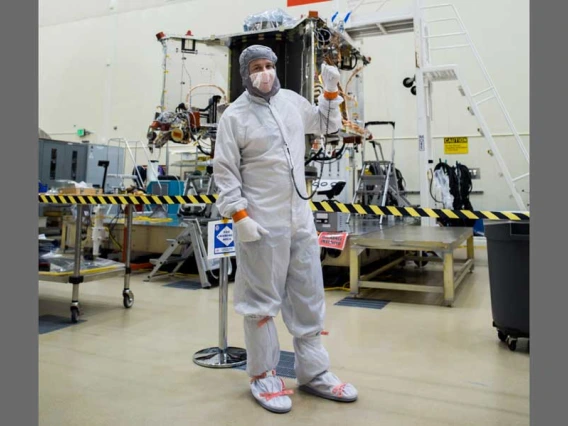 Bradley Williams in a white safety suit in front of a spacecraft.