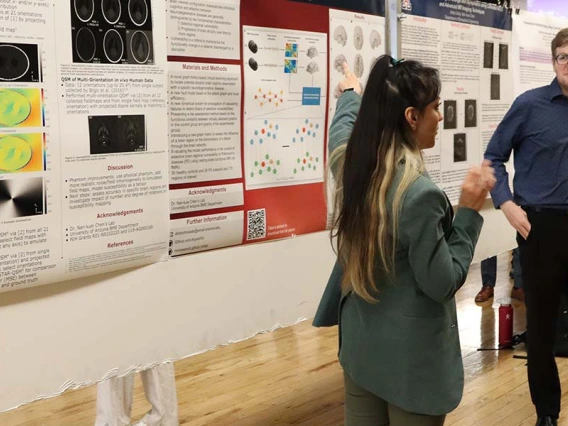 A student gestures at a research poster while two other people look on