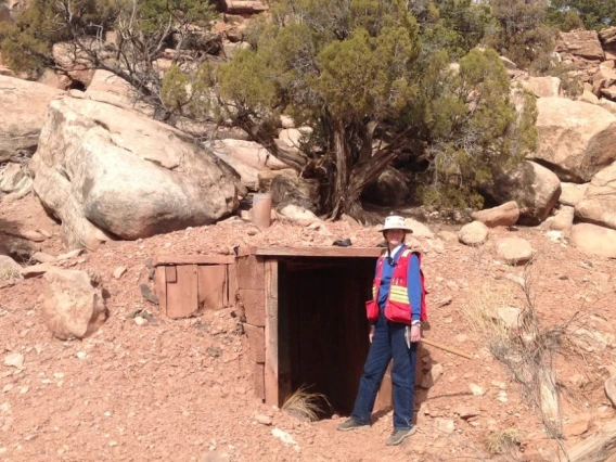 Isabel Barton wearing a red vest and standing next to the entrance of a mine in a desert setting.