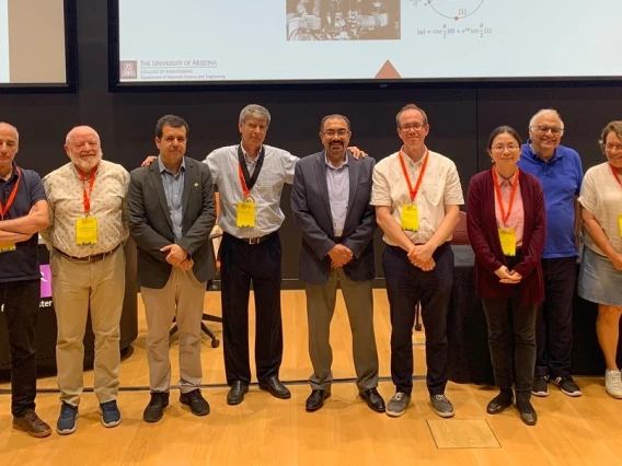 Nine people, most of whom are wearing conference lanyards, pose for a photo.