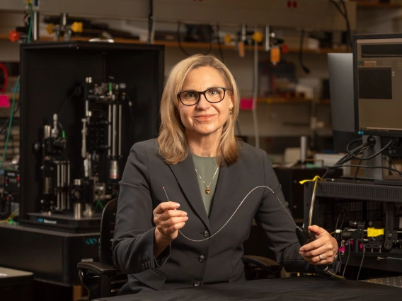 Jennifer Barton in her lab, holding a falloposope, which looks like a thin wire about 1.5 feet long.