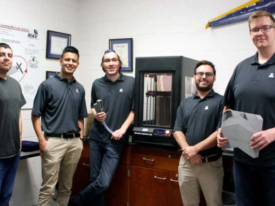 Five students standing by a 3D printer