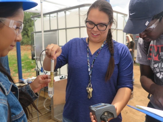 A woman, center, holds a device into a vial of water, while people on either side of her watch.