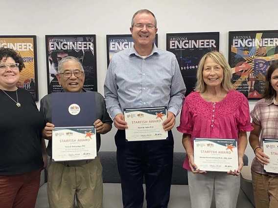 Five people stand indoors with certificates