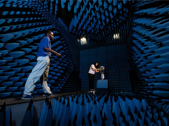 Two young men stand in a room covered in spikes of blue foam on all four walls, the floor and ceiling.