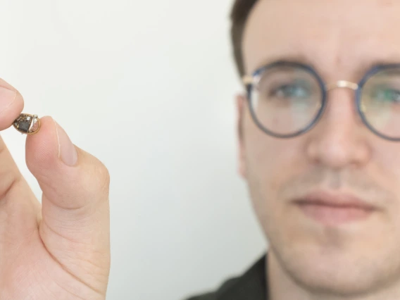 A man holds up a tiny electronic device, about the size of a chocolate chip.