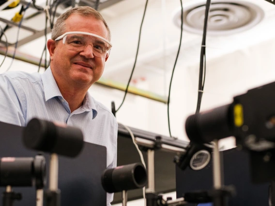 David Hahn smiling and wearing safety glasses, leaned over optics equipment