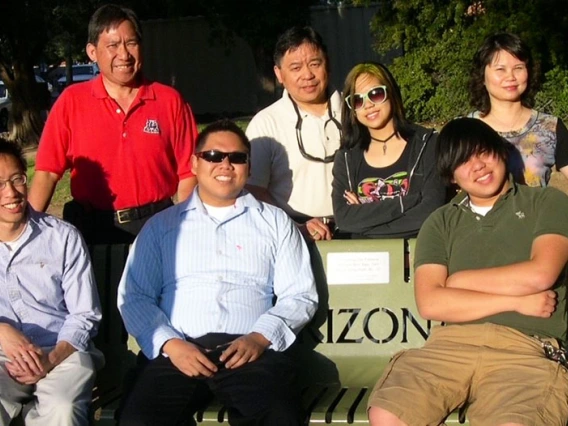 A family group of 7 gathers around a memorial bench on the University of Arizona campus