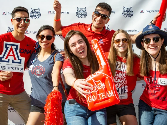 A group of people in Arizona Wildcats gear holding up an inflated #1 finger, pom poms and a UArizona Engineering logo