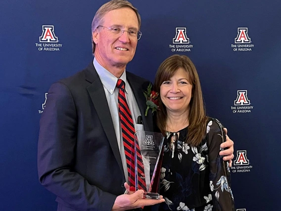 Mike and Sheri Hummel in front of a UA backdrop with a glass award