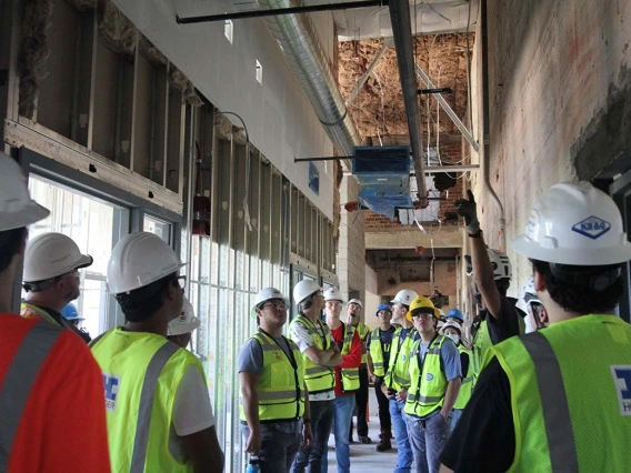 a group of students in hard hats tour an indoor construction site