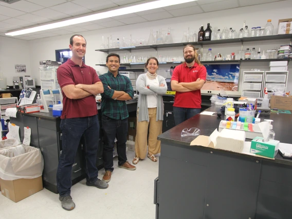 Four people stand with their arms crossed, smiling, in a chemistry laboratory.