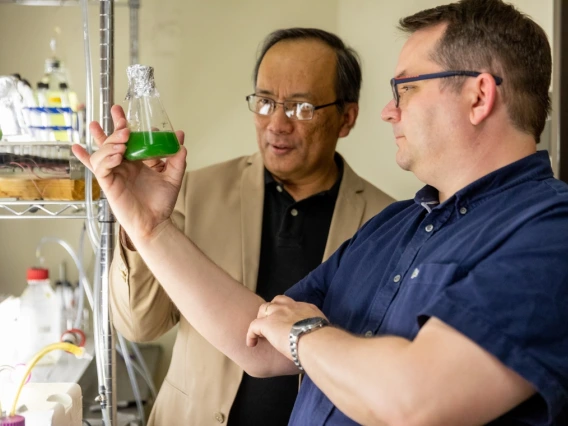 Two men examine a beaker of algae.