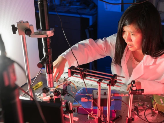 Judith Su wearing a white labcoat and leaned over a complicated array of sensors.