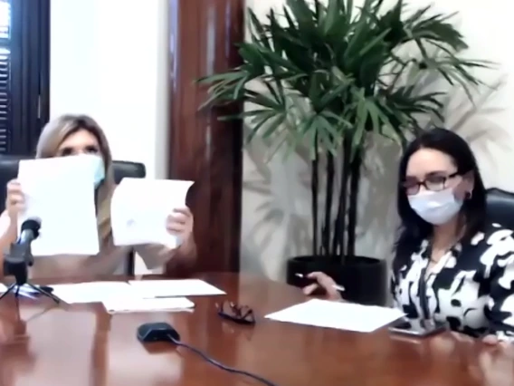 Blurry screencap of a Zoom meeting, in which two women wearing masks sit at a large table.