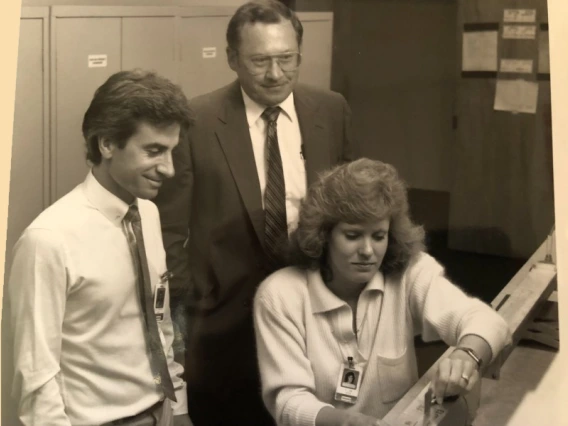 Black and white photo of two men and a woman leaned over a computer