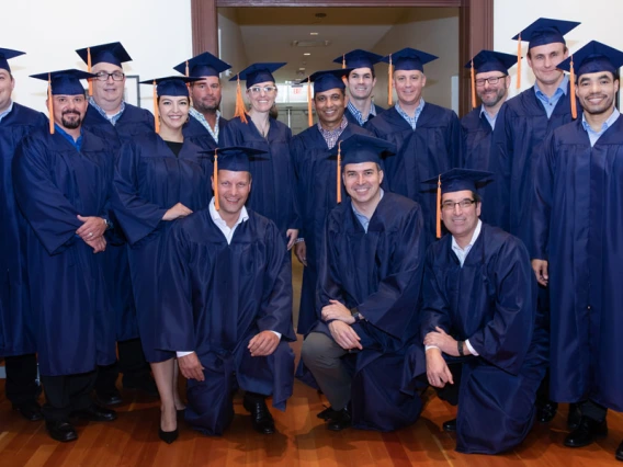 A group of 15 men and women wearing blue graduation caps and gowns