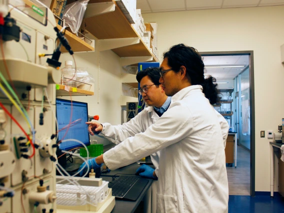 Two researchers in white lab coats look at a computer screen.