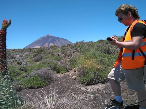A young man in an orange vests stands in an area with volcanic rock.