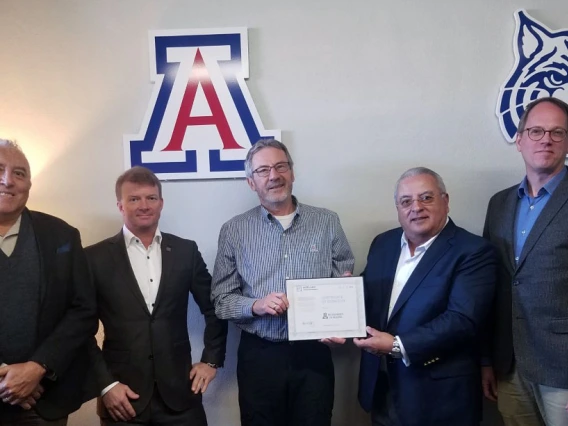 Five men stand in front of a wall with a University of Arizona block A and wildcat logo on it.