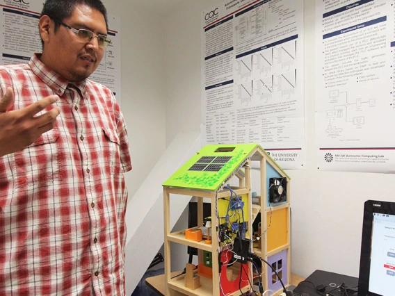 A student stands in front of a house model outfitted with electronic sensors and hooked to a monitor