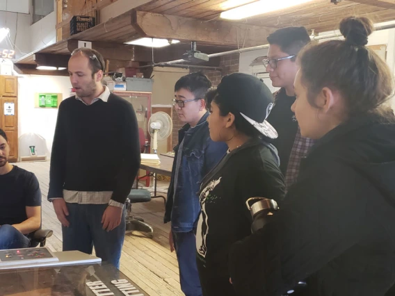 A group of students gather around to watch a demonstration.