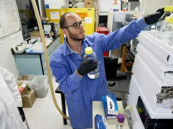 Two men in a laboratory reach for water samples setting on top of a machine.