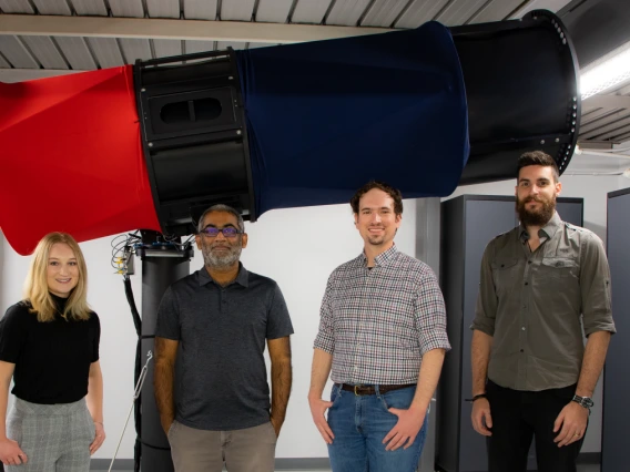 Four people stand in front of a large red and blue telescope.