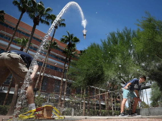 A student pulls on a rope to launch a bottle rock, which is making a big arc through the sky and back toward the ground.