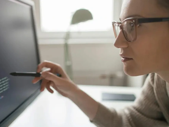 A woman leans over a computer screen, examining lines of code.