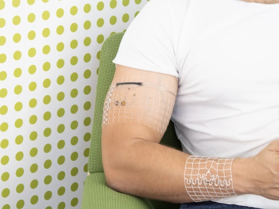 A photo of a man's torso, sitting and holding a cellphone. He has mesh bands with embedded electronics wrapped around his bicep and forearm.